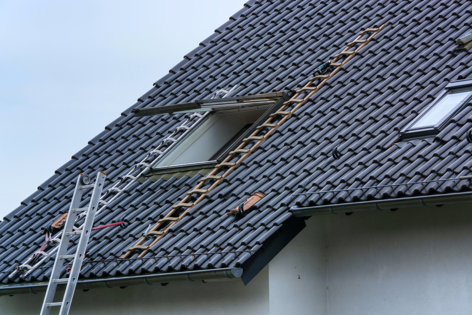 Donker pannendak met ladders en een open dakraam tijdens herstelwerken