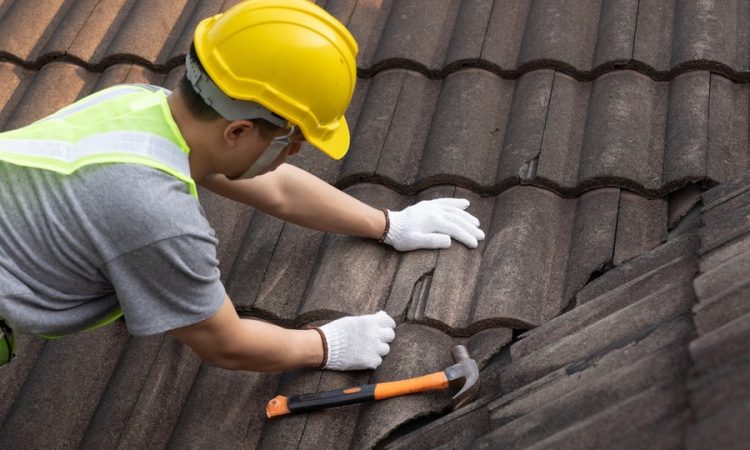 Dakwerker herstelt beschadigde dakpannen als plaatselijke herstelling bij een hellend dak - dakherstelling