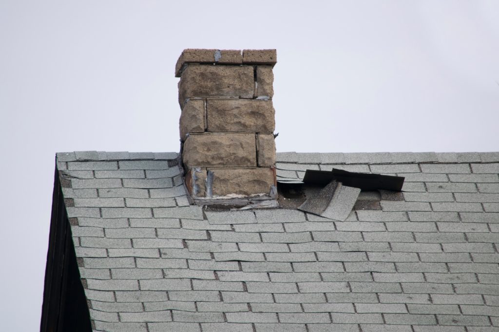 Dak met losse shingles en schade rond de schoorsteen, indicatie voor dakherstelling