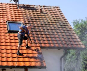 Dakwerker maakt een pannendak schoon met een hogedrukreiniger als voorbereiding op zonnepanelen