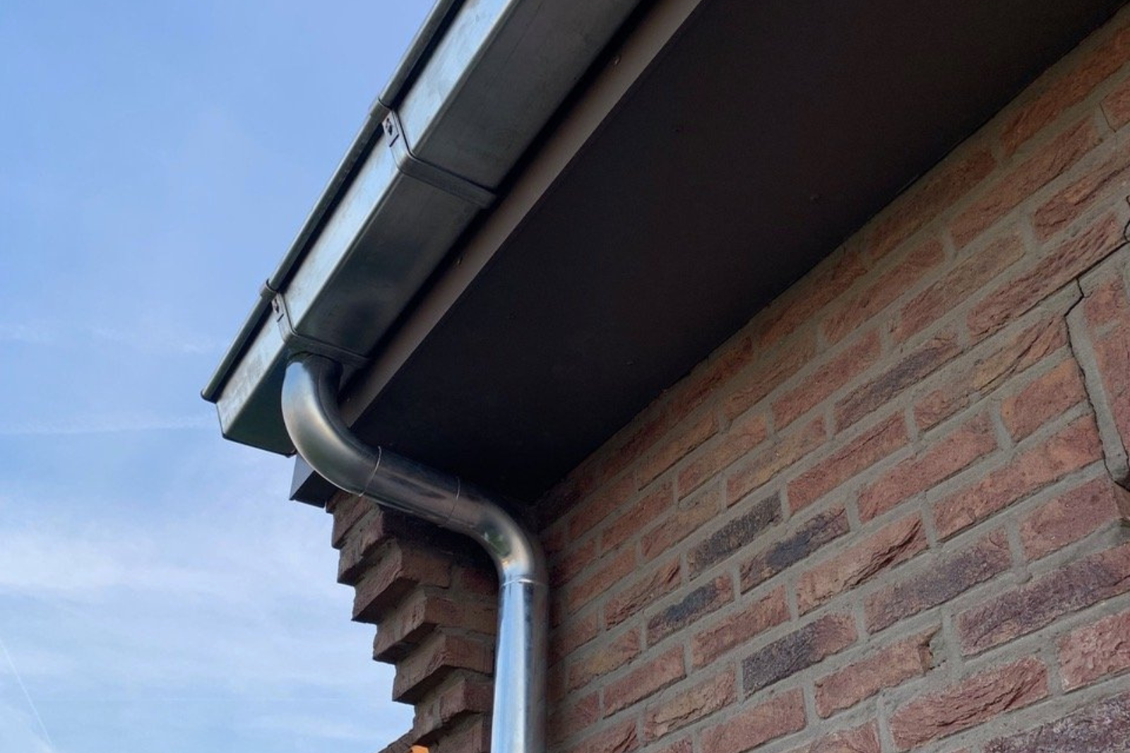 Zinken dakgoot en afvoer aan een bakstenen gevel, controleer ze na een storm